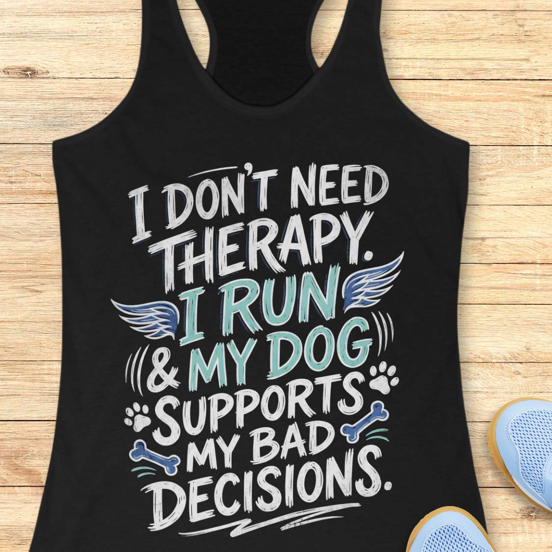 A black racerback tank top laid flat on a light wood surface, featuring a colorful graphic text that reads 'I DON'T NEED THERAPY. I RUN & MY DOG SUPPORTS MY BAD DECISIONS.