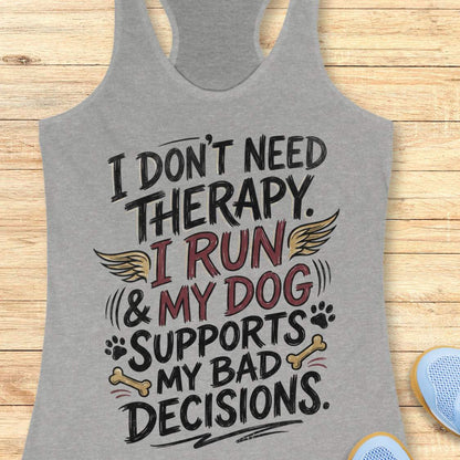 A grey racerback tank top laid flat on a light wood surface, featuring a colorful graphic text that reads 'I DON'T NEED THERAPY. I RUN & MY DOG SUPPORTS MY BAD DECISIONS.