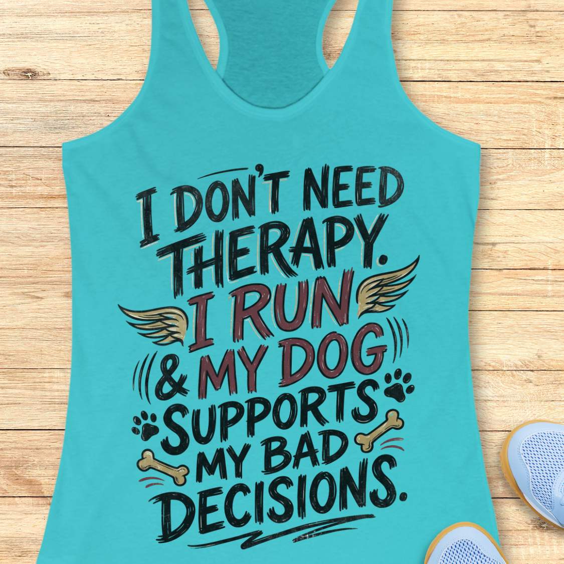 A turquoise racerback tank top laid flat on a light wood surface, featuring a colorful graphic text that reads 'I DON'T NEED THERAPY. I RUN & MY DOG SUPPORTS MY BAD DECISIONS.