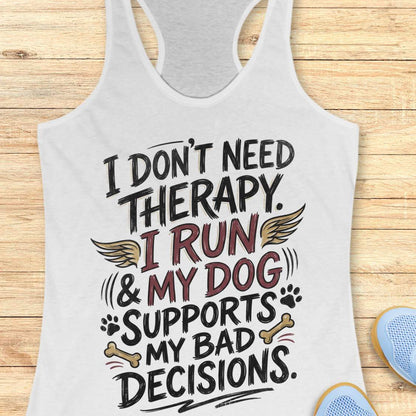A white racerback tank top laid flat on a light wood plank background, featuring a humorous graphic that reads 'I DON'T NEED THERAPY. I RUN & MY DOG SUPPORTS MY BAD DECISIONS.