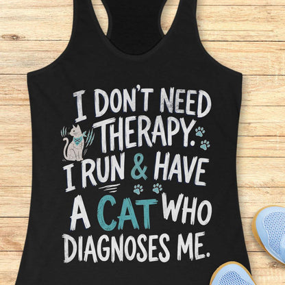 A black racerback tank top laid flat on a light wood surface, featuring a humorous graphic print with a small cat illustration and the text 'I DON'T NEED THERAPY. I RUN & HAVE A CAT WHO DIAGNOSES ME.