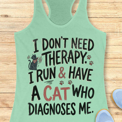 A mint green racerback tank top with a humorous graphic print, laid flat on a light wood background. The print features a black cat illustration and the text 'I DON'T NEED THERAPY.