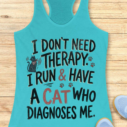 A turquoise racerback tank top laid flat on a light wood surface, featuring a humorous graphic that reads 'I DON'T NEED THERAPY. I RUN & HAVE A CAT WHO DIAGNOSES ME.