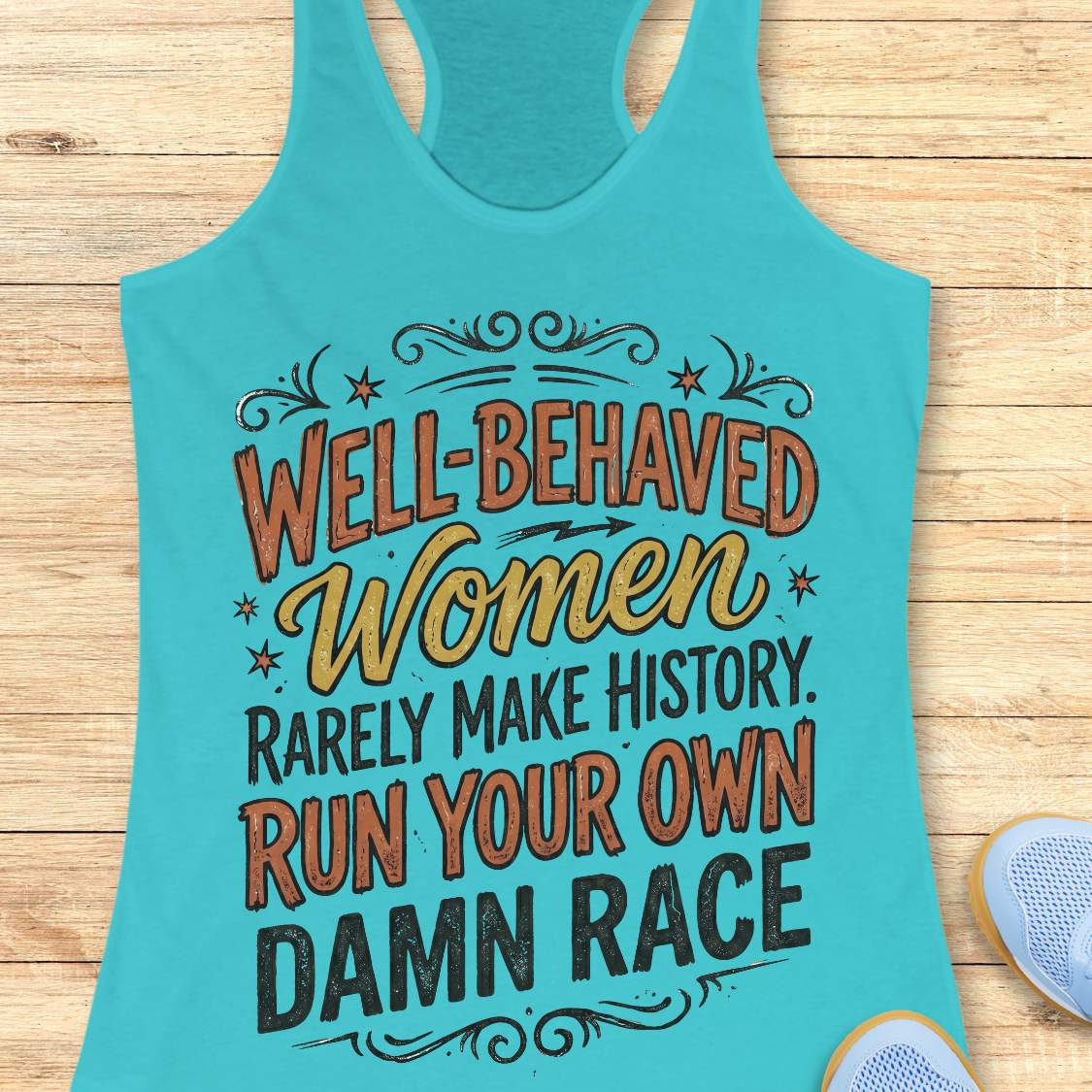 A turquoise racerback tank top laid flat on a light wood surface, featuring a motivational graphic that reads 'Well-Behaved Women Rarely Make History. Run Your Own Damn Race' in orange, yellow, and black lettering.
