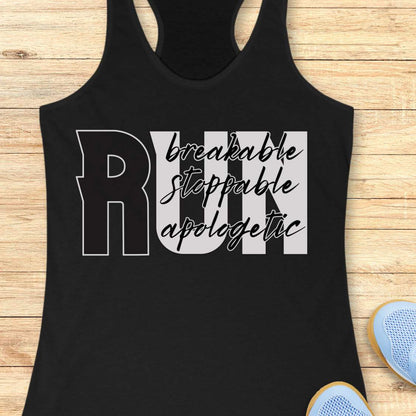 A black racerback tank top laid flat on a light wood background, featuring a large graphic that reads 'RUN' with the words 'breakable stoppable apologetic' in white and gray script across the front. Partial blue sneakers are visible at the bottom right as styling props.