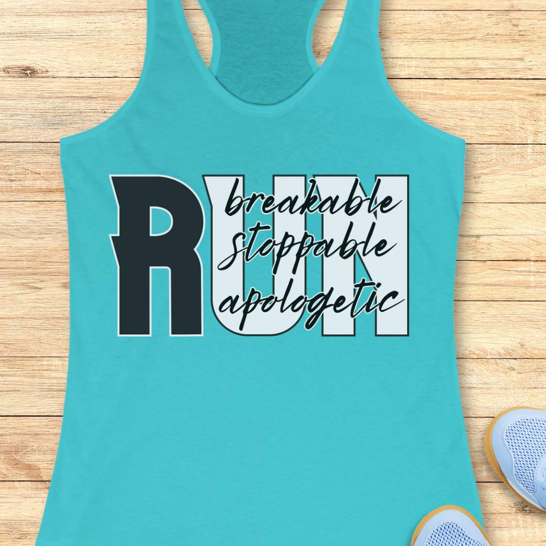 A turquoise racerback tank top laid flat on a light wood plank background, featuring a graphic print that reads 'RUN' with 'breakable stoppable apologetic' in black script and block lettering. Partial sneakers are visible at the bottom right as styling props.