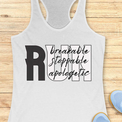 A white racerback tank top with a black graphic text print reading 'RUN breakable stoppable apologetic' laid flat on a light wood plank background. Part of a blue shoe is visible in the bottom right corner.