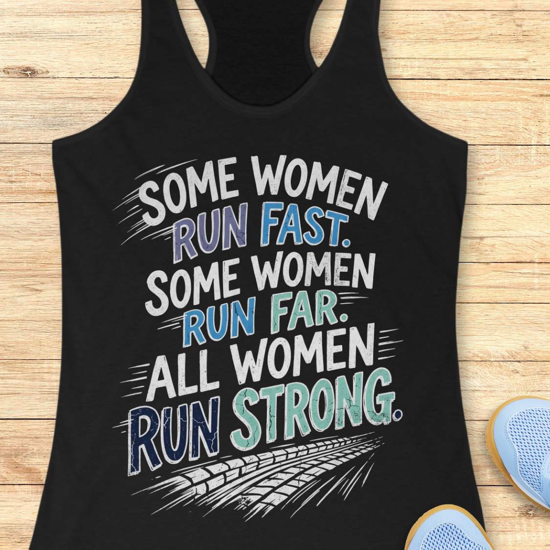 A black racerback tank top laid flat on a light wood surface, featuring a motivational graphic with illustrated sneakers.