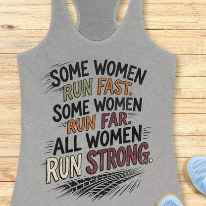 A grey racerback tank top laid flat on a light wood surface, featuring a motivational graphic with illustrated sneakers.