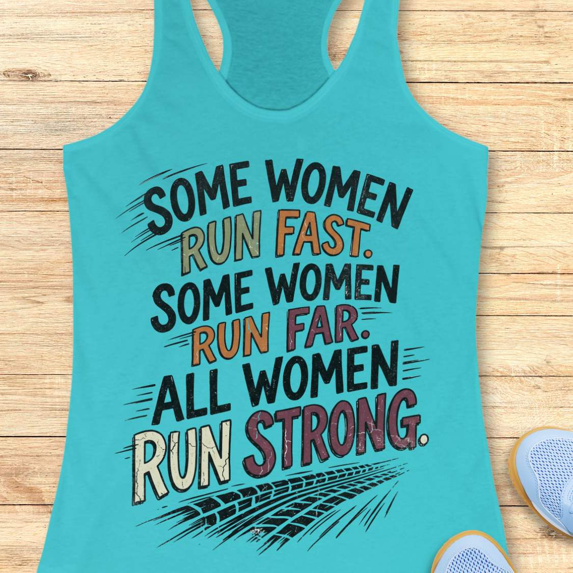 A blue racerback tank top laid flat on a light wood surface, featuring a motivational graphic with illustrated sneakers.