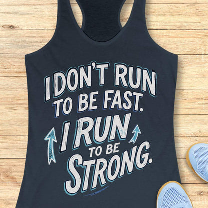 A indigo racerback tank top laid flat on a light wood surface, featuring a motivational graphic with illustrated sneakers.