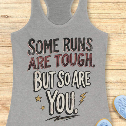 A heather grey racerback tank top laid flat on a light wood surface, featuring a motivational graphic with illustrated sneakers.