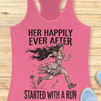 A pink racerback tank top laid flat on a light wood background, featuring a graphic of a woman running with the text 'HER HAPPILY EVER AFTER STARTED WITH A RUN'.