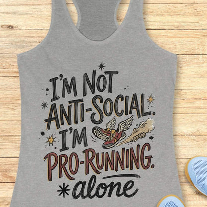 A heather gray racerback tank top laid flat on a light wood background, featuring a graphic that reads 'I'M NOT ANTI-SOCIAL. I'M PRO-RUNNING.