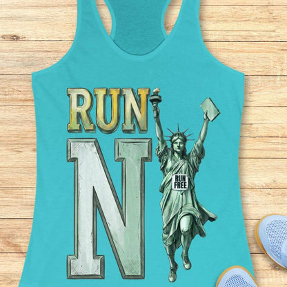 A turquoise racerback tank top laid flat on a light wood surface, featuring a large graphic that reads "RUN N" with a Statue of Liberty illustration and a small "RUN FREE" sign. Partial light blue sneakers are visible at the bottom right as styling props.