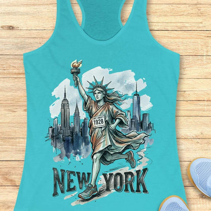 A turquoise racerback tank top laid flat on a light wood surface, featuring a graphic of the Statue of Liberty running with the New York City skyline behind her and the text 'NEW YORK' at the bottom. Partial light blue shoes are visible at the bottom right corners.