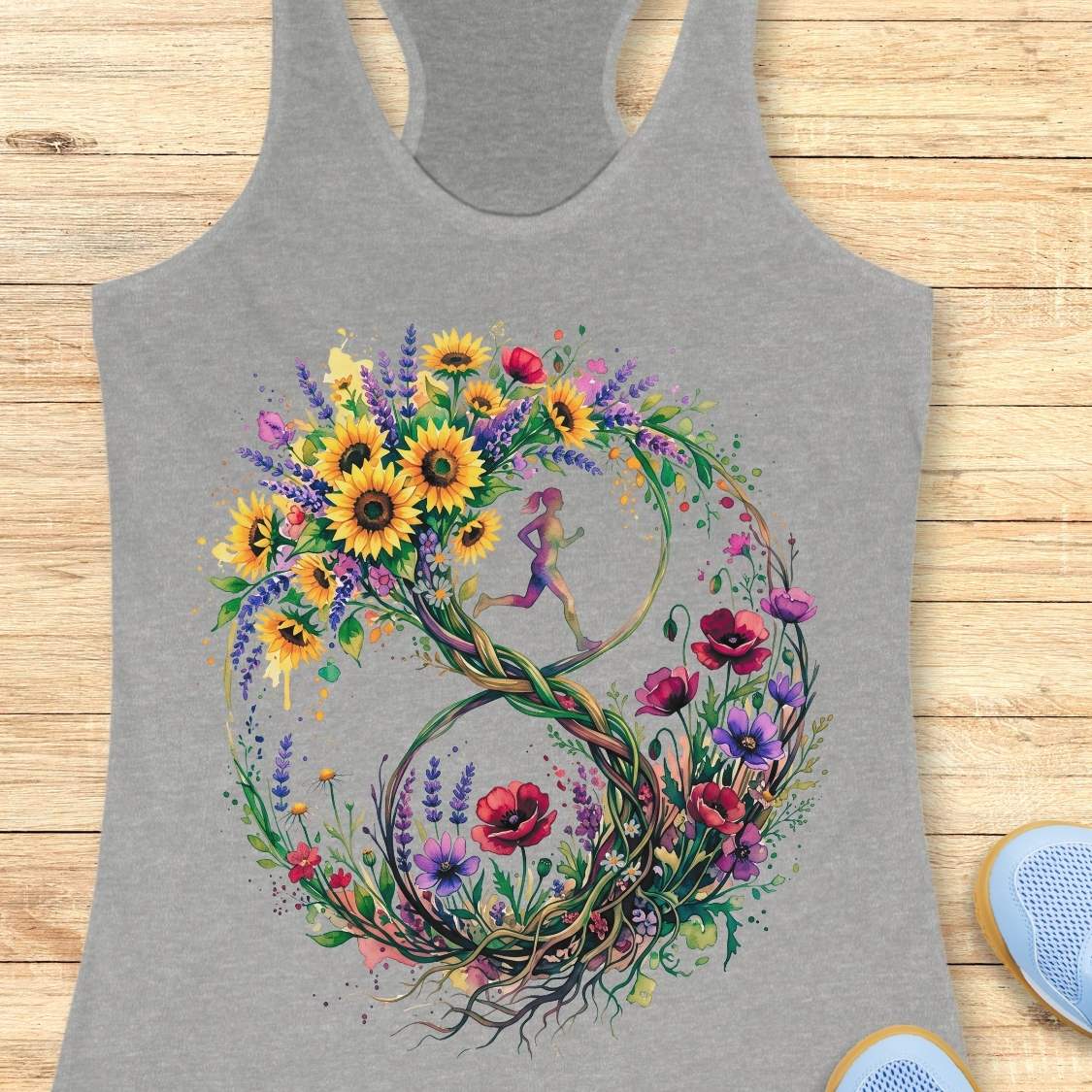 A heather gray racerback tank top featuring a large, colorful graphic of a stylized number 8 formed by wildflowers and a small running girl in the center, laid flat on a light wood background.