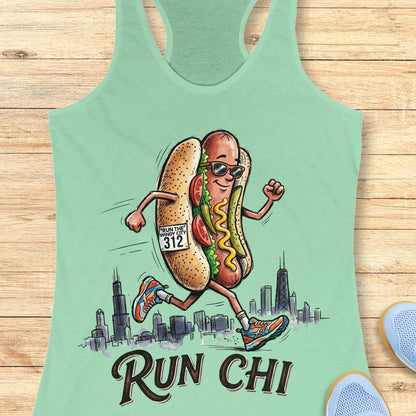 Mint green women's racerback tank top featuring a playful illustration of a running hot dog wearing sunglasses and colorful running shoes. The hot dog has a race bib that reads “RUN THE WINDY CITY 312” and is jogging in front of a hand-drawn Chicago skyline. The design includes classic Chicago-style hot dog toppings such as tomatoes, pickles, mustard, and relish. Large text below the illustration reads: “RUN CHI.” The artwork combines running humor with Chicago pride in a fun, cartoon-style design.