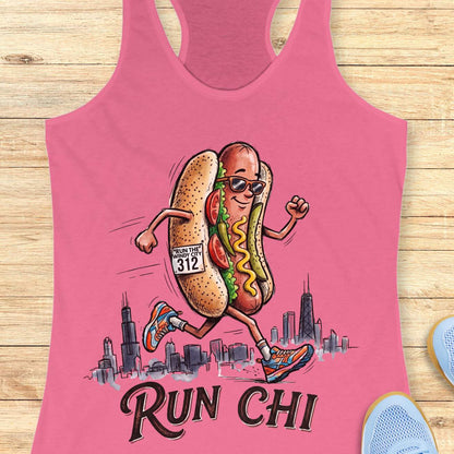 pink women's racerback tank top featuring a playful illustration of a running hot dog wearing sunglasses and colorful running shoes. The hot dog has a race bib that reads “RUN THE WINDY CITY 312” and is jogging in front of a hand-drawn Chicago skyline. The design includes classic Chicago-style hot dog toppings such as tomatoes, pickles, mustard, and relish. Large text below the illustration reads: “RUN CHI.” The artwork combines running humor with Chicago pride in a fun, cartoon-style design.