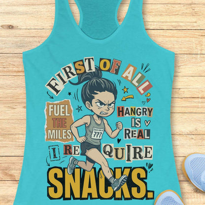 blue racerback tank top featuring a cartoon runner wearing a race bib and running shoes, surrounded by bold typography. The design reads: “First of all, fuel the miles. Hangry is real. I require snacks.” The artwork uses a playful mix of fonts, yellow, black, beige, and coral accents, with doodle-style arrows, stars, and hearts. The tank top is displayed on a light wood surface with running shoes partially visible in the corners.