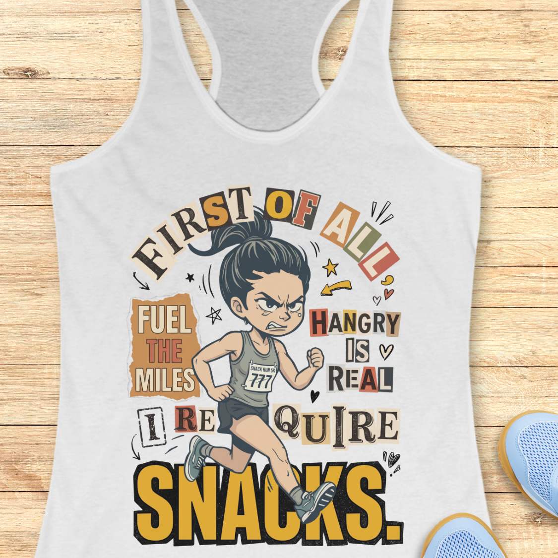 white racerback tank top featuring a cartoon runner wearing a race bib and running shoes, surrounded by bold typography. The design reads: “First of all, fuel the miles. Hangry is real. I require snacks.” The artwork uses a playful mix of fonts, yellow, black, beige, and coral accents, with doodle-style arrows, stars, and hearts. The tank top is displayed on a light wood surface with running shoes partially visible in the corners.