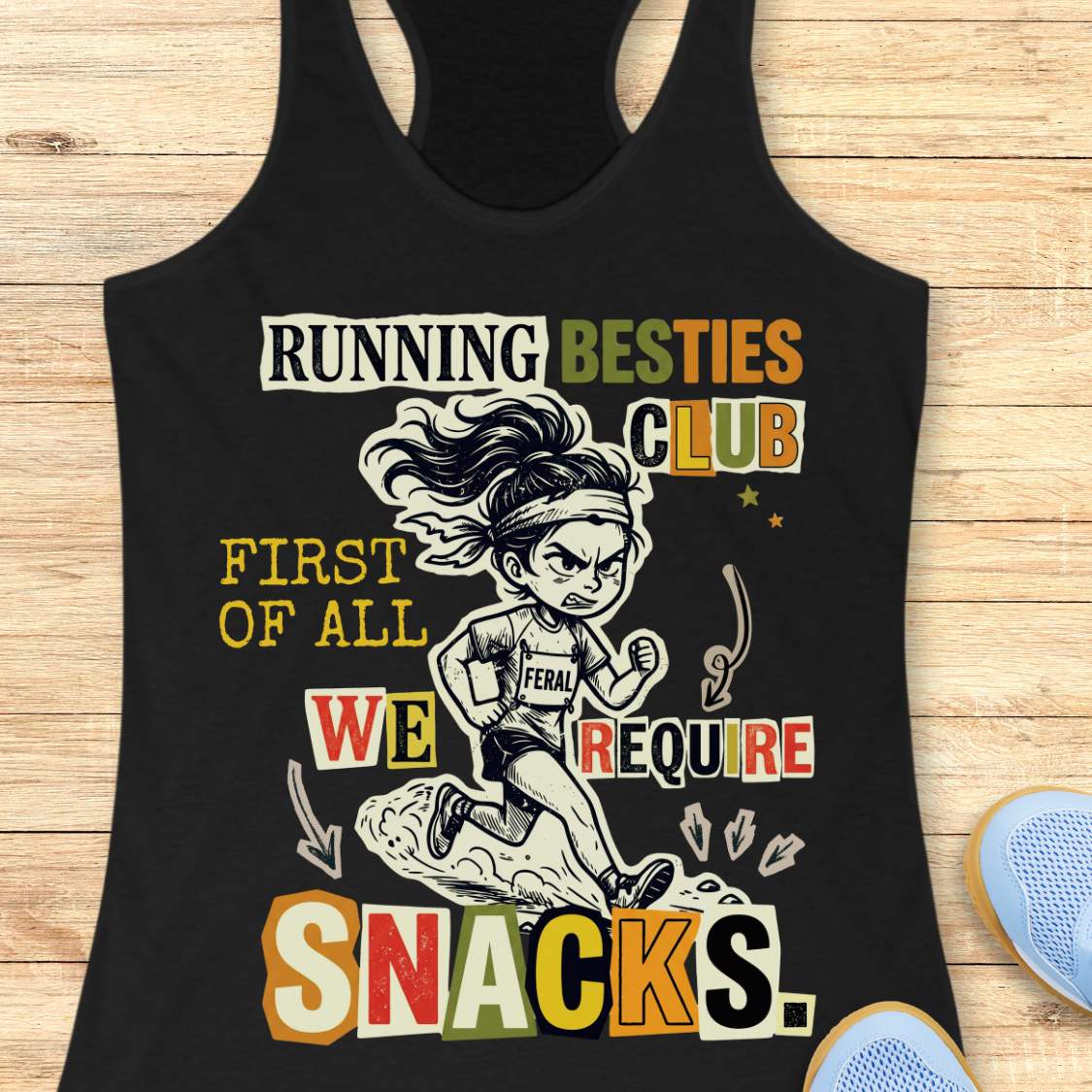A black racerback tank top laid flat on a light wood background, featuring a colorful graphic of a cartoon female runner and the text 'RUNNING BESTIES CLUB FIRST OF ALL WE REQUIRE SNACKS.'.