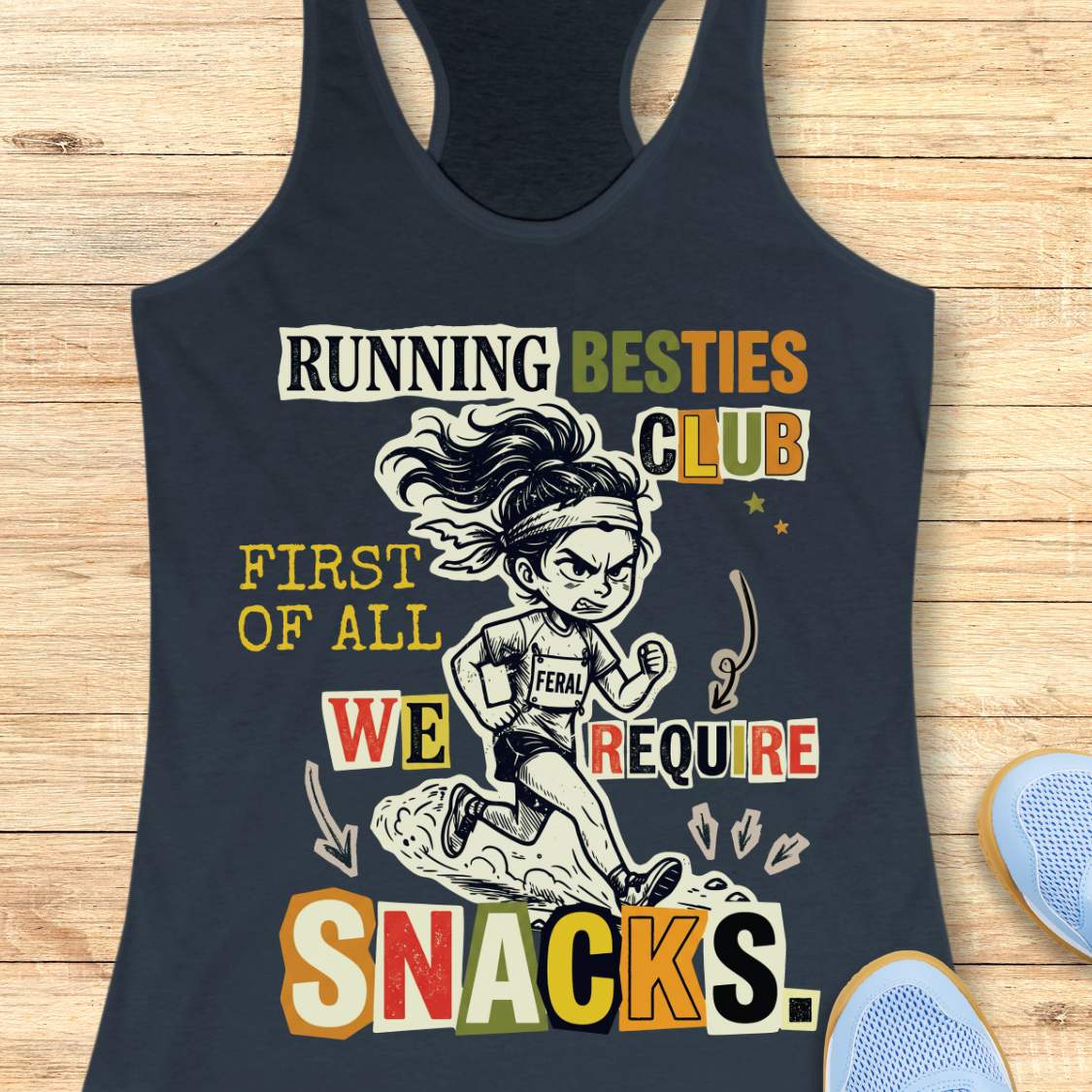A indigo racerback tank top with a colorful graphic print on a light wood background. The graphic features a cartoon illustration of a female runner and the text 'RUNNING BESTIES CLUB FIRST OF ALL WE REQUIRE SNACKS.