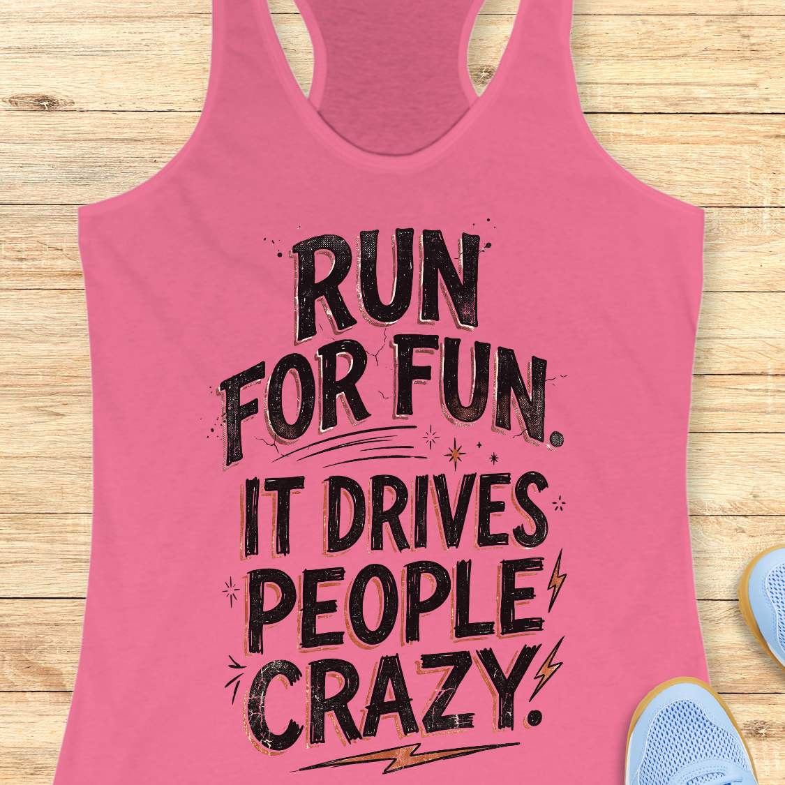 pink racerback tank top featuring a bold typographic running design. The text reads: “Run for fun. It drives people crazy.” in distressed black lettering with vintage-style shading. Decorative elements include stars, sparkles, curved accent lines, and lightning bolts. The tank top is displayed flat on a light wood background with partial blue running shoes visible in the lower corners.