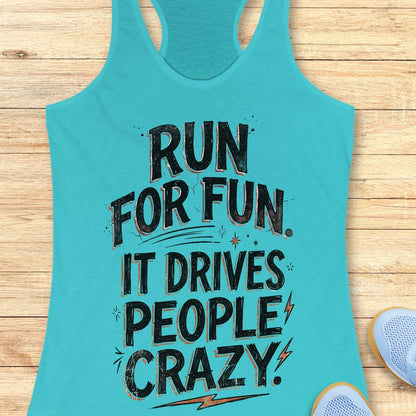 blue racerback tank top featuring a bold typographic running design. The text reads: “Run for fun. It drives people crazy.” in distressed black lettering with vintage-style shading. Decorative elements include stars, sparkles, curved accent lines, and lightning bolts. The tank top is displayed flat on a light wood background with partial blue running shoes visible in the lower corners.
