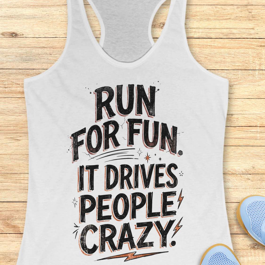 white racerback tank top featuring a bold typographic running design. The text reads: “Run for fun. It drives people crazy.” in distressed black lettering with vintage-style shading. Decorative elements include stars, sparkles, curved accent lines, and lightning bolts. The tank top is displayed flat on a light wood background with partial blue running shoes visible in the lower corners.