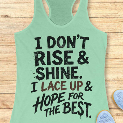 Mint green racerback tank top featuring a bold, distressed typography design that reads: “I DON’T RISE & SHINE. I LACE UP & HOPE FOR THE BEST.” The text is displayed in a mix of black and brown brush-style lettering, creating a playful and relatable message for runners who prefer determination over morning enthusiasm. The humorous running-themed design is ideal for athletes, joggers, and fitness enthusiasts.