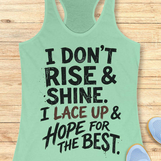 Mint green racerback tank top featuring a bold, distressed typography design that reads: “I DON’T RISE & SHINE. I LACE UP & HOPE FOR THE BEST.” The text is displayed in a mix of black and brown brush-style lettering, creating a playful and relatable message for runners who prefer determination over morning enthusiasm. The humorous running-themed design is ideal for athletes, joggers, and fitness enthusiasts.