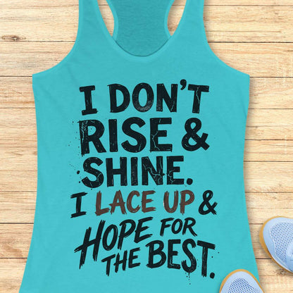 blue racerback tank top featuring a bold, distressed typography design that reads: “I DON’T RISE & SHINE. I LACE UP & HOPE FOR THE BEST.” The text is displayed in a mix of black and brown brush-style lettering, creating a playful and relatable message for runners who prefer determination over morning enthusiasm. The humorous running-themed design is ideal for athletes, joggers, and fitness enthusiasts.