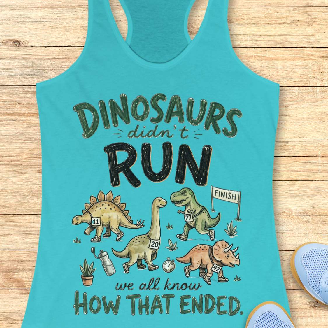 blue racerback tank top featuring the humorous running-themed phrase, “DINOSAURS didn’t RUN we all know HOW THAT ENDED.” The design includes cartoon dinosaurs wearing race bibs and running shoes, jogging toward a finish line. Small race-themed elements such as a water bottle, stopwatch, and plants add detail to the playful illustration. The fun, motivational graphic combines running humor with a lighthearted take on prehistoric extinction, making it ideal for runners and fitness enthusiasts.