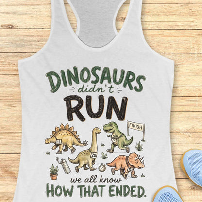 white racerback tank top featuring the humorous running-themed phrase, “DINOSAURS didn’t RUN we all know HOW THAT ENDED.” The design includes cartoon dinosaurs wearing race bibs and running shoes, jogging toward a finish line. Small race-themed elements such as a water bottle, stopwatch, and plants add detail to the playful illustration. The fun, motivational graphic combines running humor with a lighthearted take on prehistoric extinction, making it ideal for runners and fitness enthusiasts.