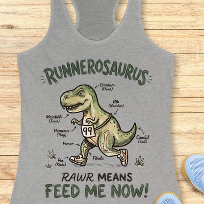 grey racerback tank top featuring a playful dinosaur running graphic and the phrase, “RUNNEROSAURUS RAWR MEANS FEED ME NOW!” The design shows a cartoon T-Rex wearing running shoes and race bib number 99, illustrated like an anatomy diagram with humorous labels such as “Cranium (Head),” “Mandible (Jaws),” “Humerus (Tiny),” “Pes (Kicks),” and “Caudal (Tail).” The lighthearted running-themed artwork combines dinosaur humor with runner culture, making it a fun choice for runners, joggers, and dinosaur ent
