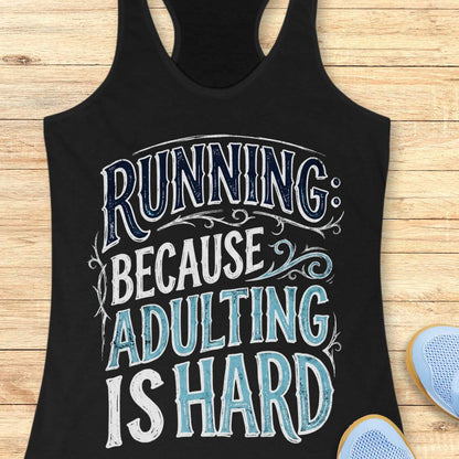 A black racerback tank top laid flat on a light wood background, featuring a large distressed graphic that reads 'RUNNING BECAUSE ADULTING IS HARD' in white and light blue lettering. Partial blue sneakers are visible at the bottom right as styling props.