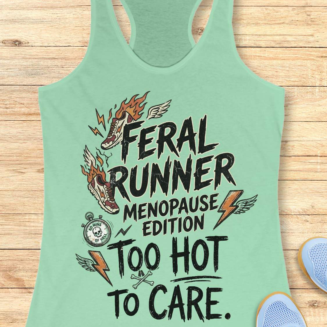 A mint green racerback tank top laid flat on a light wood background, featuring a humorous graphic for 'Feral Runner Menopause Edition' with a flaming shoe, stopwatch, lightning bolts, and the phrase 'Too Hot to Care.'.