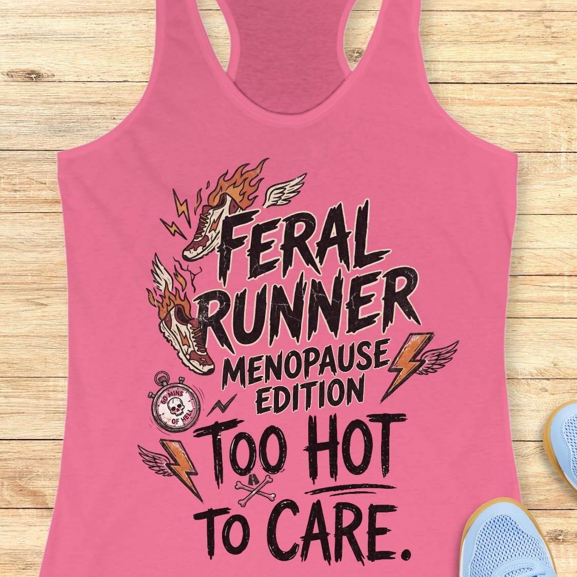 A pink racerback tank top laid flat on a light wood background, featuring a humorous graphic that reads 'Feral Runner Menopause Edition Too Hot to Care' with illustrated shoes, lightning bolts, wings, and a stopwatch.
