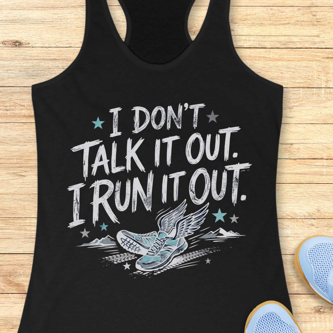 A black racerback tank top laid flat on a light wood background, featuring a distressed white graphic that reads 'I DON'T TALK IT OUT. I RUN IT OUT.