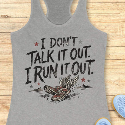 A heather gray racerback tank top laid flat on a light wood background, featuring a graphic print with the text 'I DON'T TALK IT OUT. I RUN IT OUT.