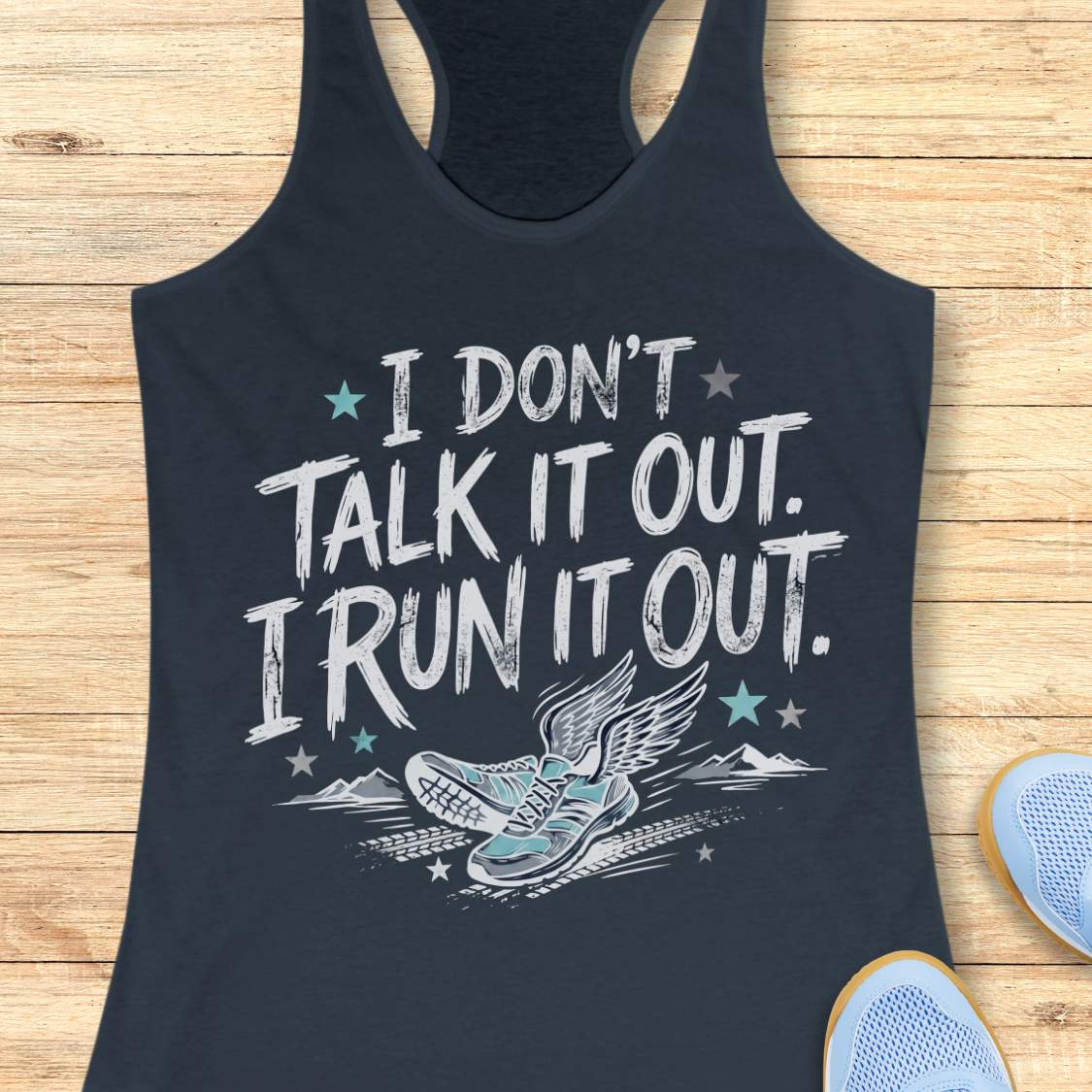A indigo racerback tank top laid flat on a light wood background, featuring a distressed white graphic that reads 'I DON'T TALK IT OUT. I RUN IT OUT.