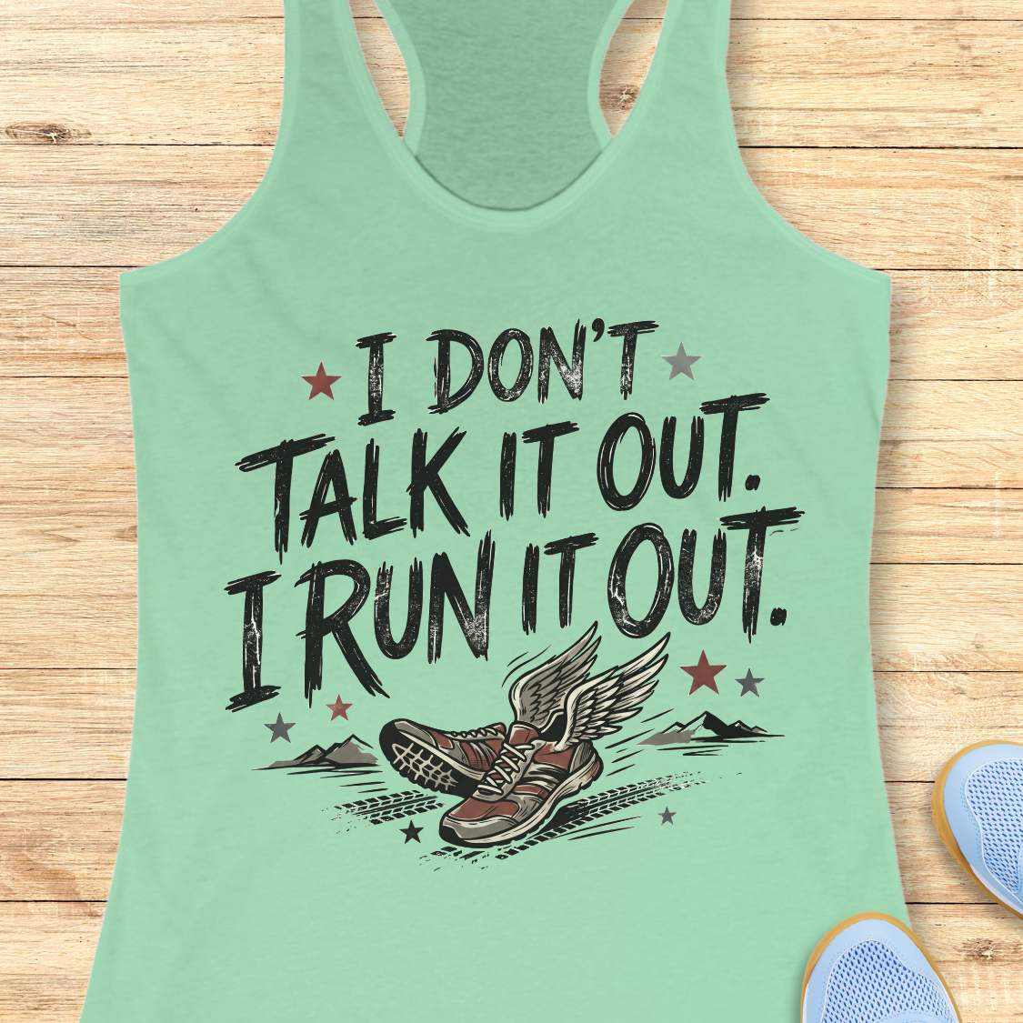 A mint green racerback tank top laid flat on a light wood background, featuring a distressed black graphic that reads 'I DON'T TALK IT OUT. I RUN IT OUT.