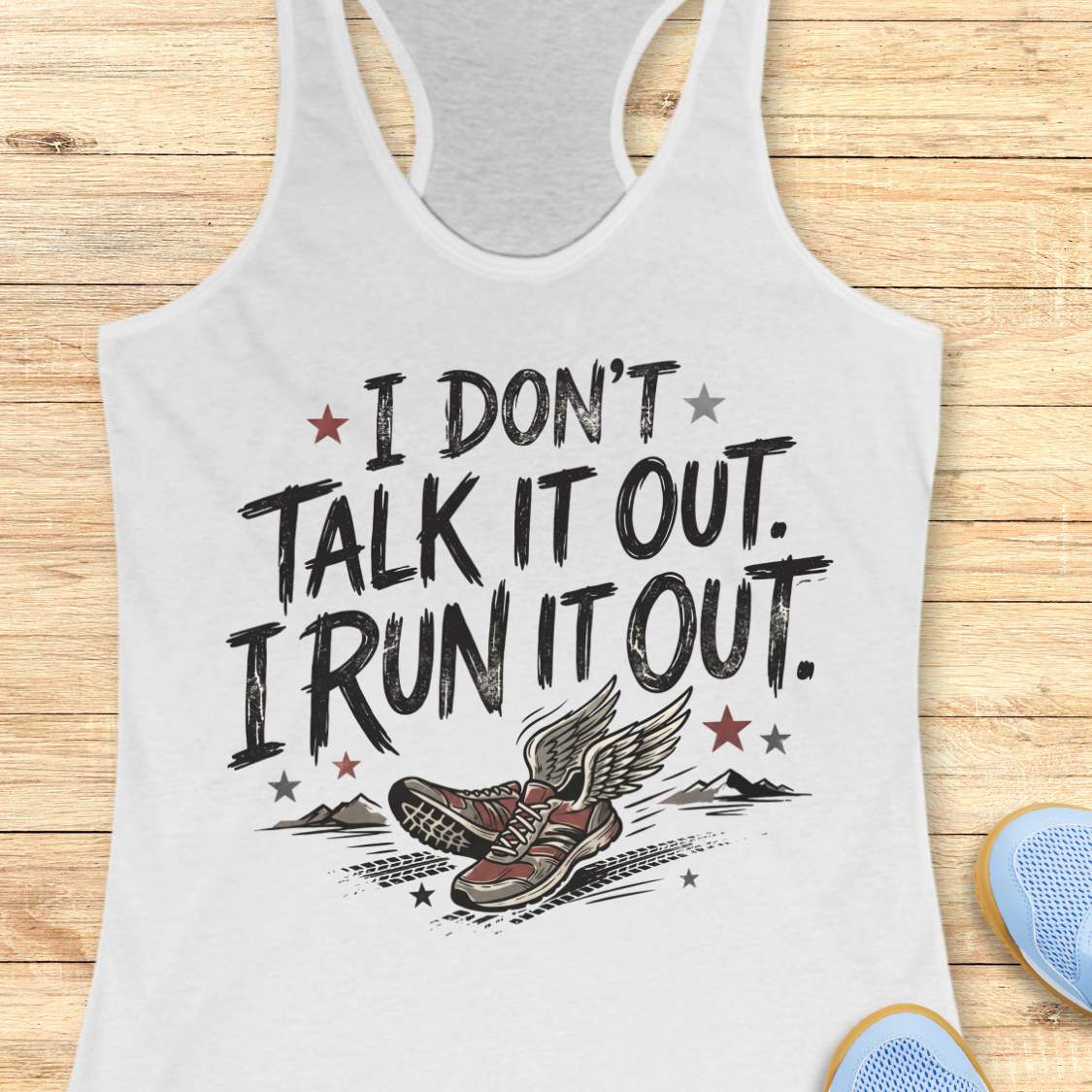 A white racerback tank top laid flat on a light wood plank background, featuring a graphic print that reads 'I DON'T TALK IT OUT. I RUN IT OUT.