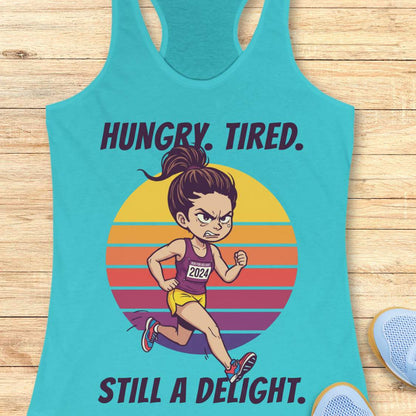 A turquoise racerback tank top laid flat on a light wood surface, featuring a cartoon runner graphic with the text 'HUNGRY. TIRED.  Still a delight.'