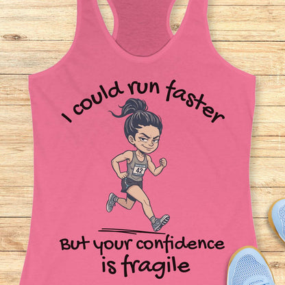 A pink racerback tank top laid flat on a light wood background, featuring a cartoon runner graphic and the text 'I could run faster But your confidence is fragile'.