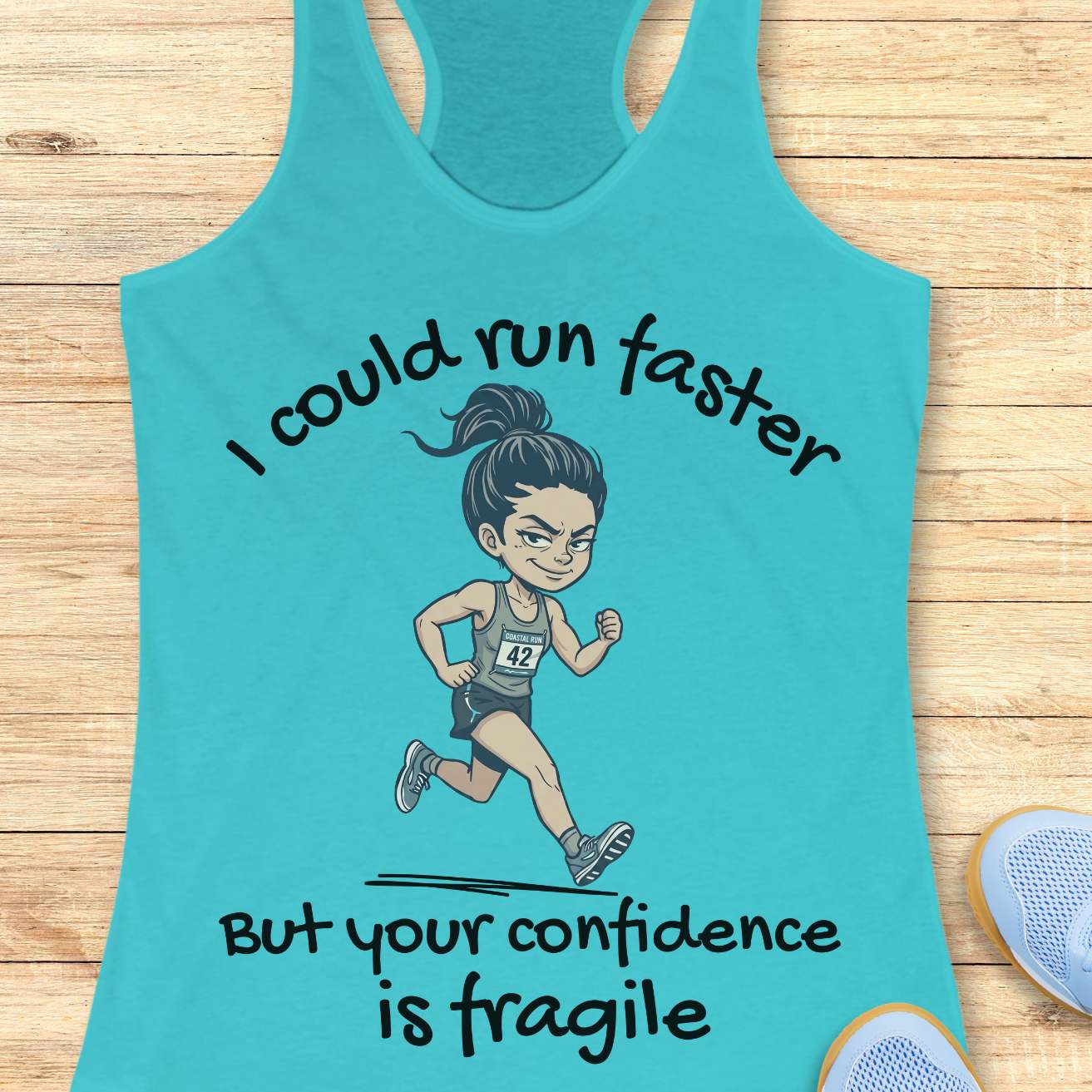 A turquoise racerback tank top laid flat on a light wood surface, featuring a cartoon runner graphic and the text 'I could run faster But your confidence is fragile.' Partial blue shoes are visible at the bottom right as styling props.