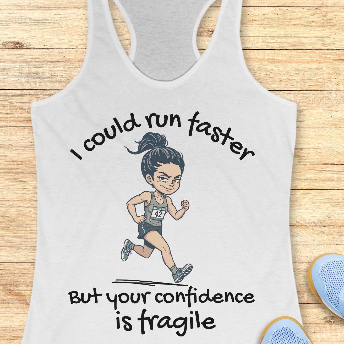 A white racerback tank top laid flat on a light wood background, featuring a cartoon illustration of a female runner and the text 'I could run faster But your confidence is fragile'. Partial blue shoes are visible at the bottom right as styling props.