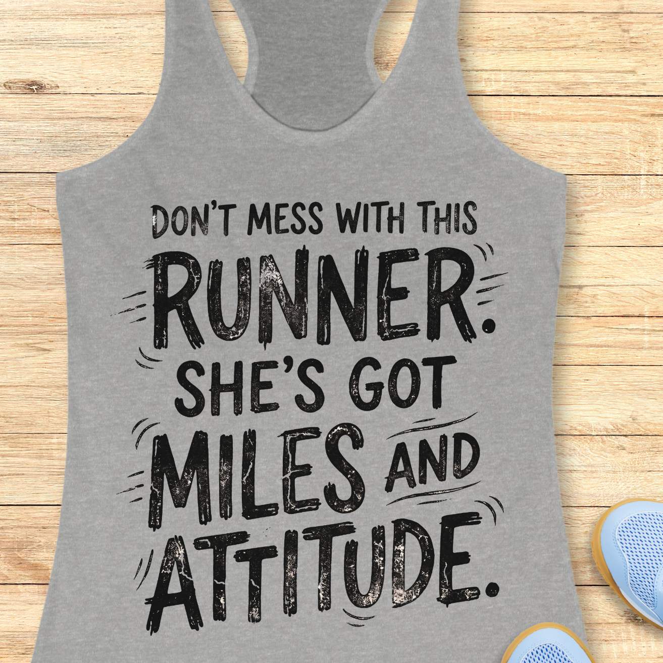 A heather gray racerback tank top with a black distressed typographic print reading 'DON'T MESS WITH THIS RUNNER. SHE'S GOT MILES AND ATTITUDE.
