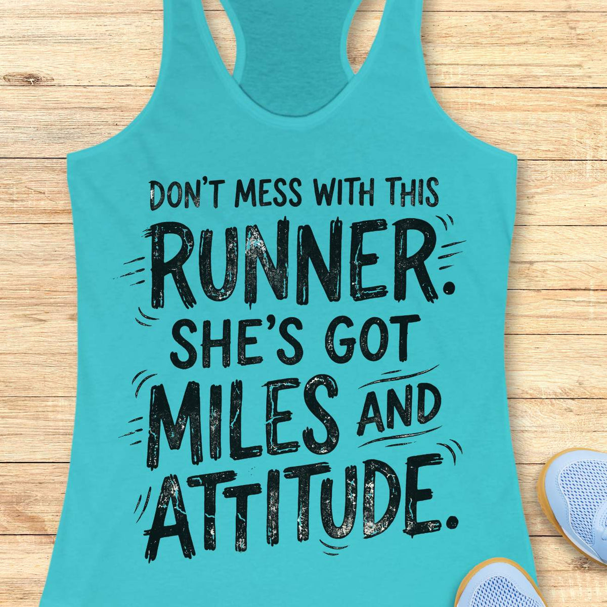 A turquoise racerback tank top with a black distressed text graphic reading 'DON'T MESS WITH THIS RUNNER. SHE'S GOT MILES AND ATTITUDE.